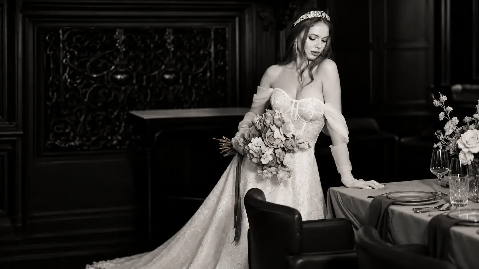 Bride in a white wedding dress with a white bridal bouquet beside a set table in an elegant interior — Sanjski šopek