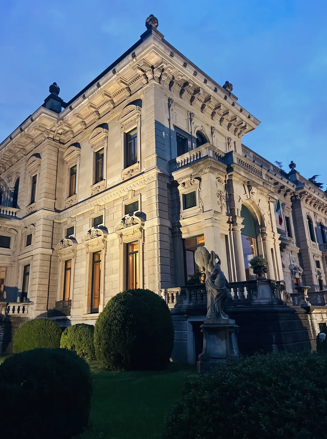 Osvetljena fasada Ville Erba pod modrim večernim nebom ob jezeru Como.