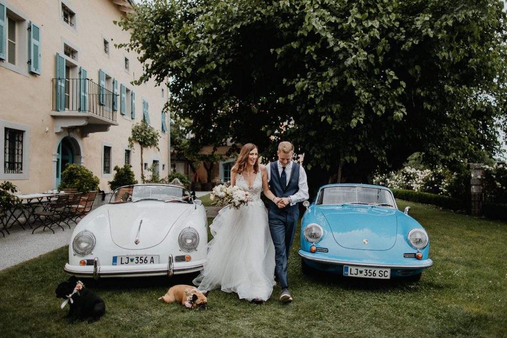 Ženin in nevesta ob poročnih avtomobilih.