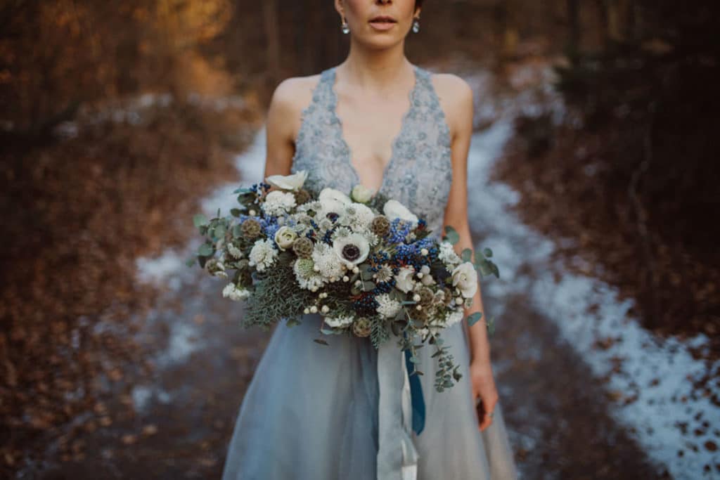 Nevesta v modri poročni obleki in z zimskim poročnim šopkom