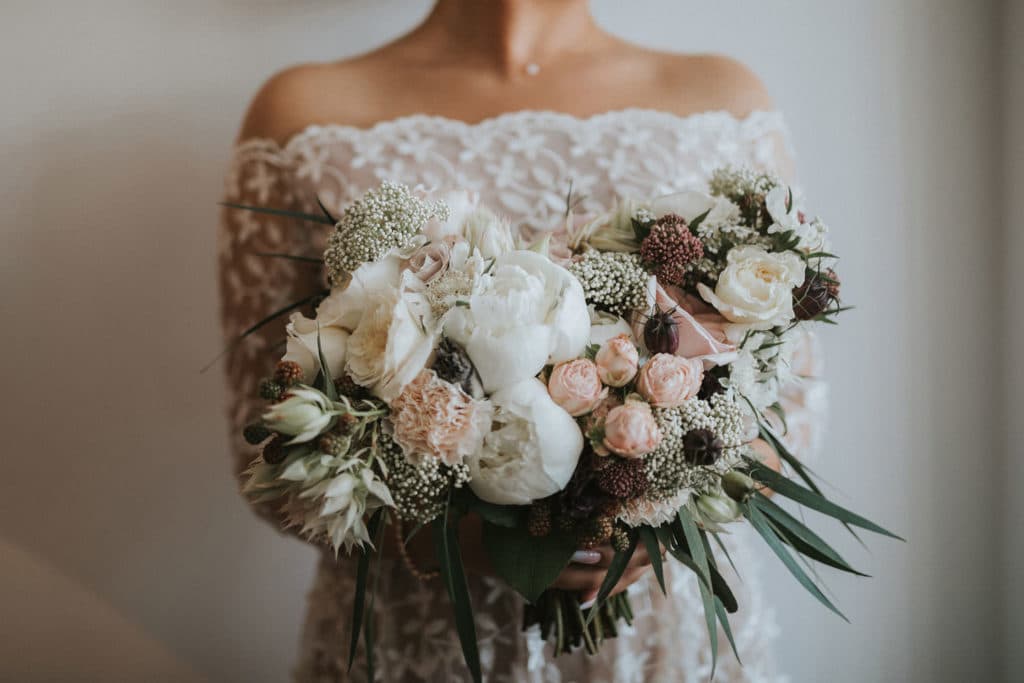 Nevesta drži eleganten poročni šopek s potonikami in angleškimi vrtnicami