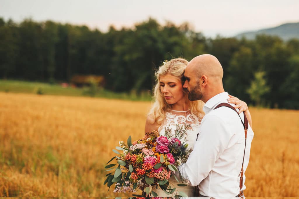 Nevesta in ženin stojita v objemu na travniku z divjim poročnim šopkom